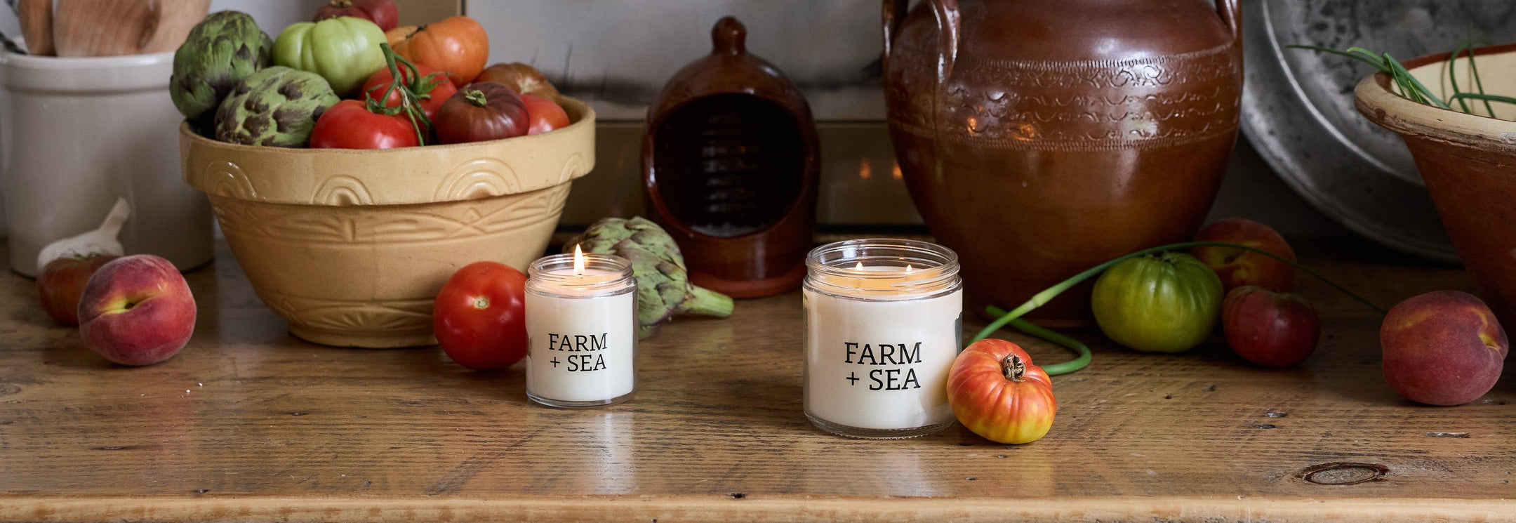 Farm + Sea Classic Candle in both sizes on a wooden counter top with summer produce