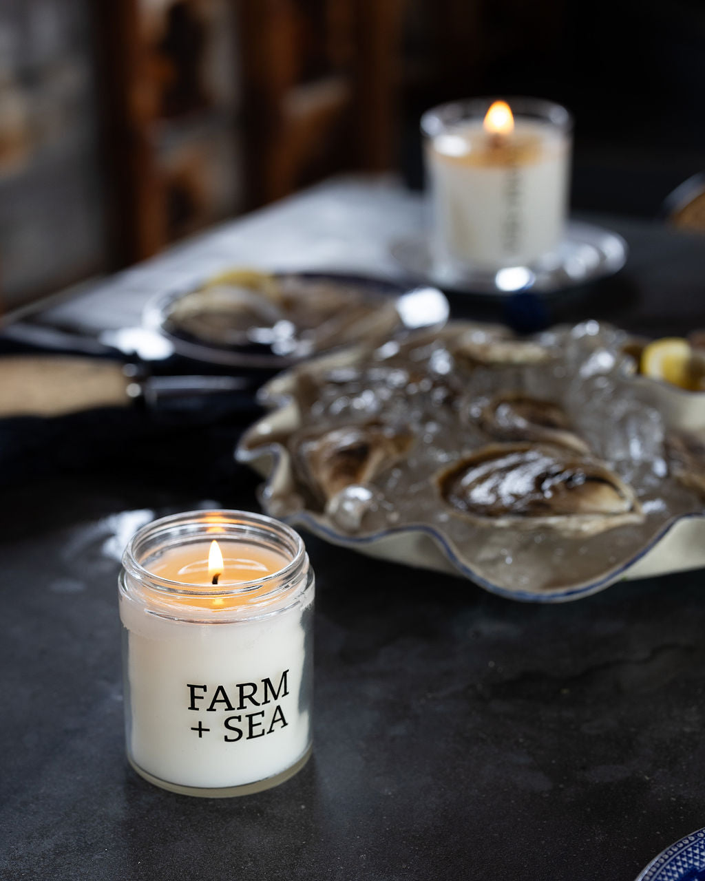 Farm + Sea small classic candle on table with oysters in the background.