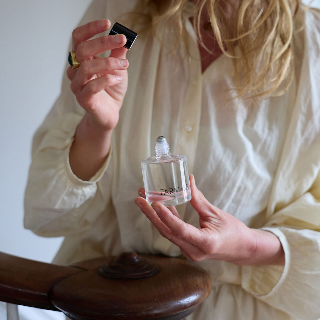 Woman in a linen dress holding a bottle of Farm + Sea perfume with a blurred background