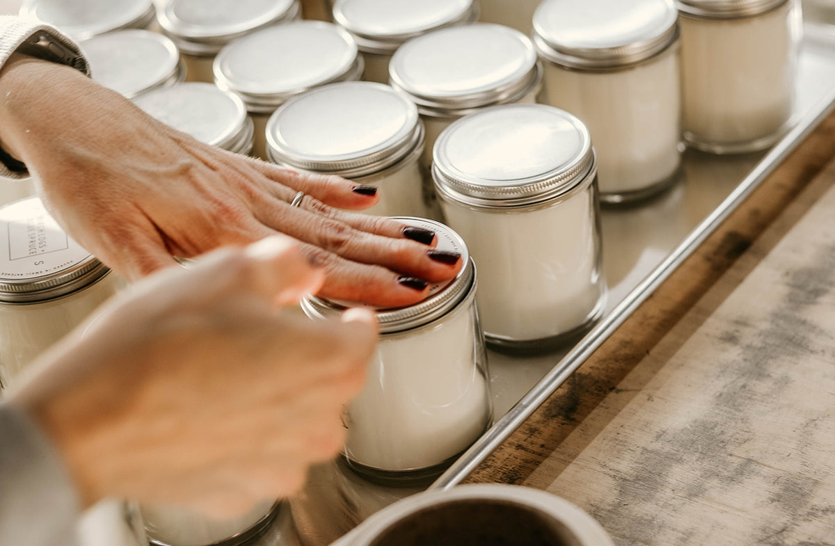 Mary Swenson, Farm + Sea founder, labeling classic candle jars on a tray with a wooden surface underneath.