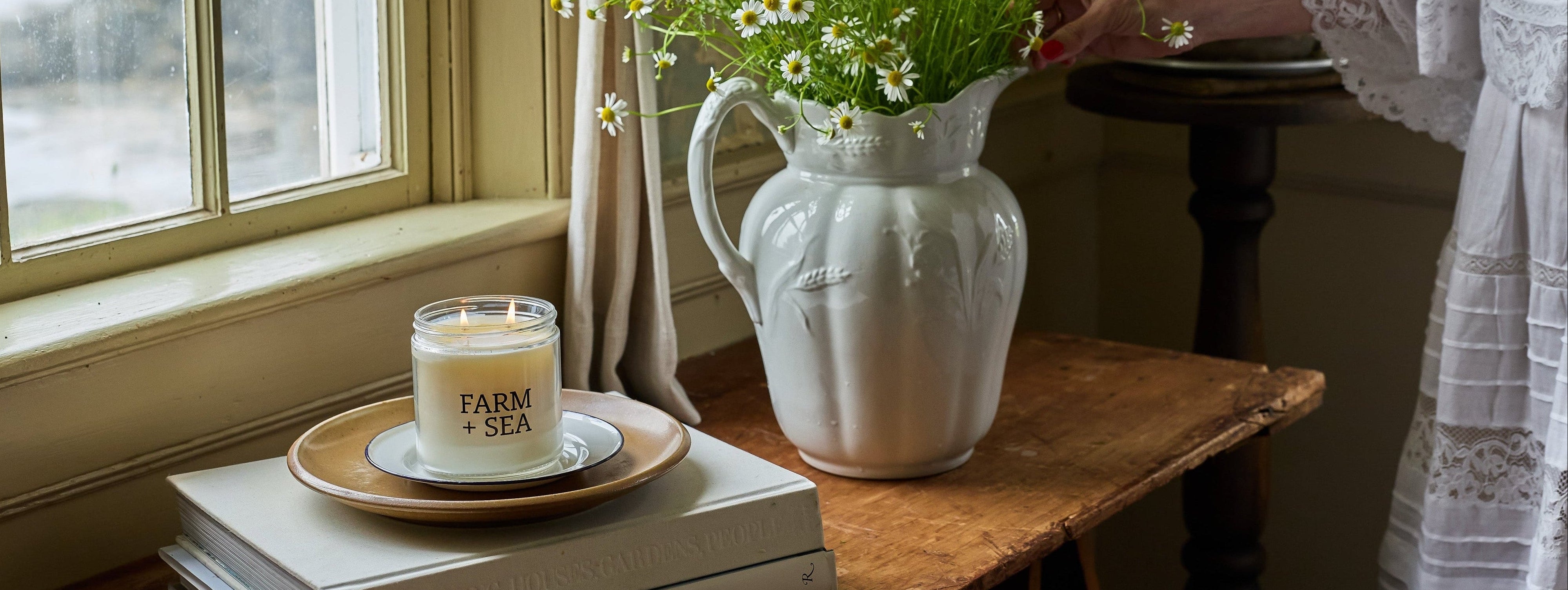 Farm + Sea Classic Candle on a rustic wooden table next to a window at a beach house