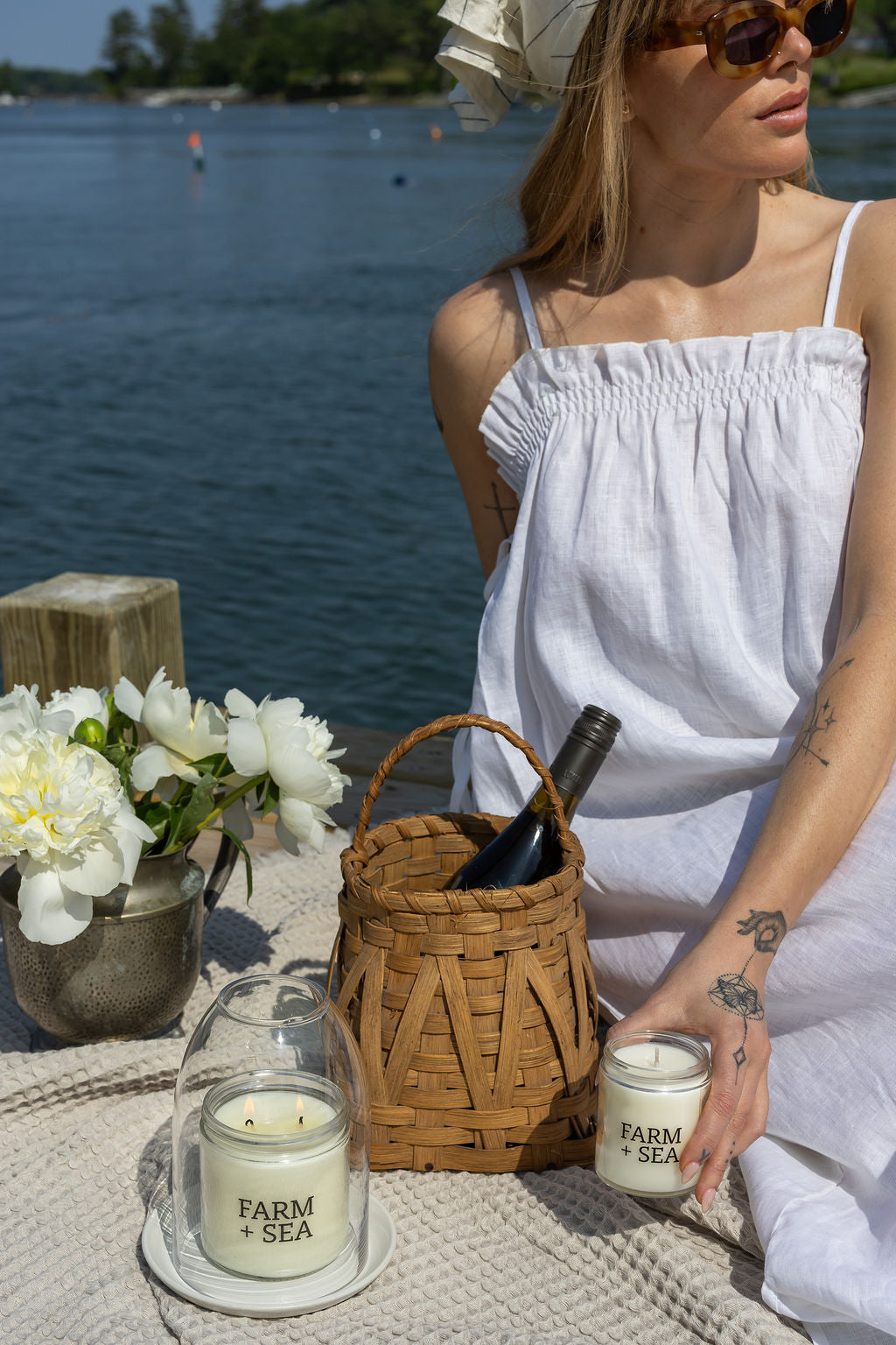 Woman in white dress by the ocean with Farm + Sea classic candles and a basket