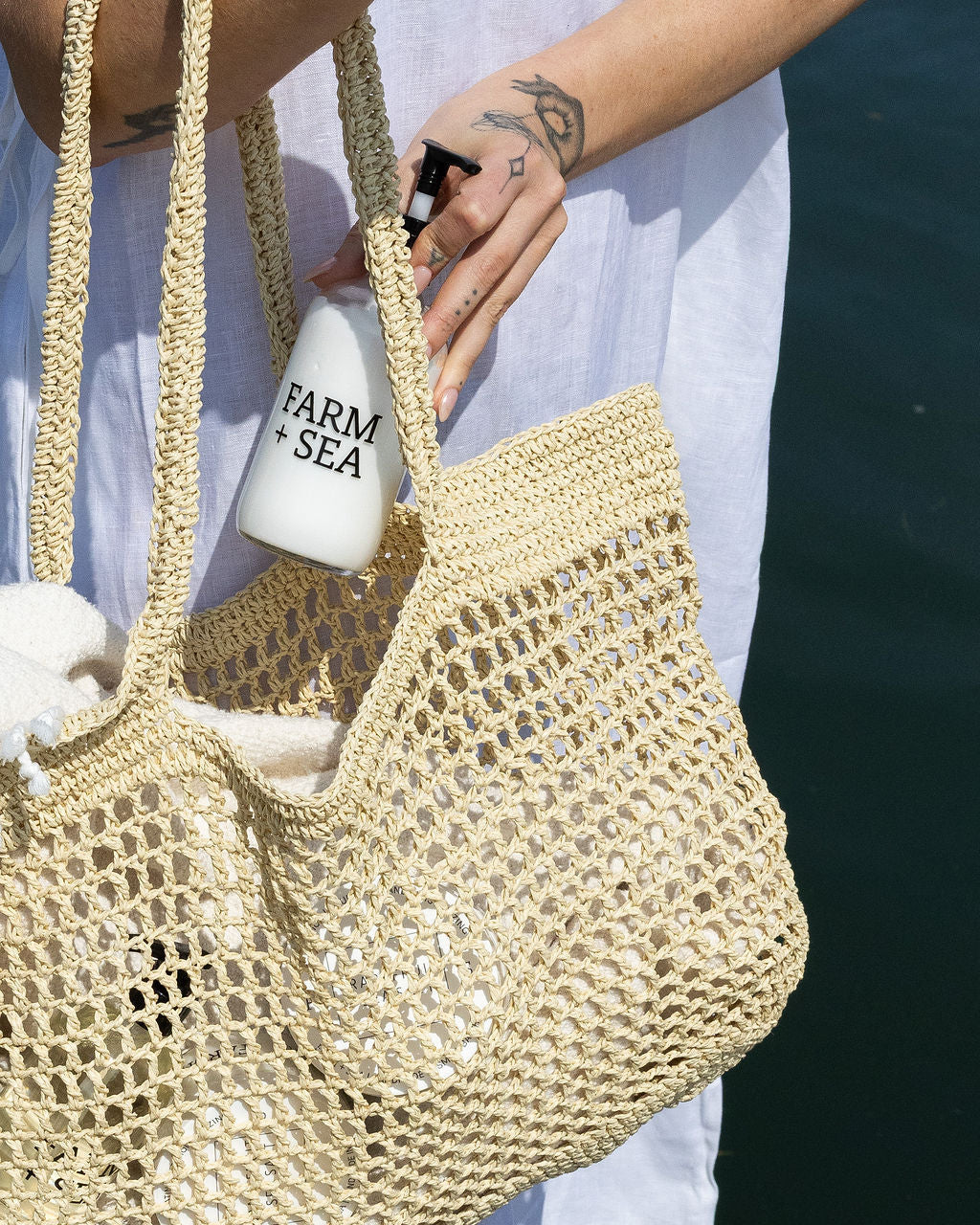 Woman holding a woven bag with a bottle of Farm + Sea body lotion.